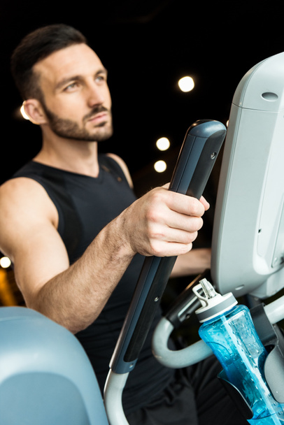 selective focus of sport bottle near athletic man working out on exercise bike  - Photo, Image