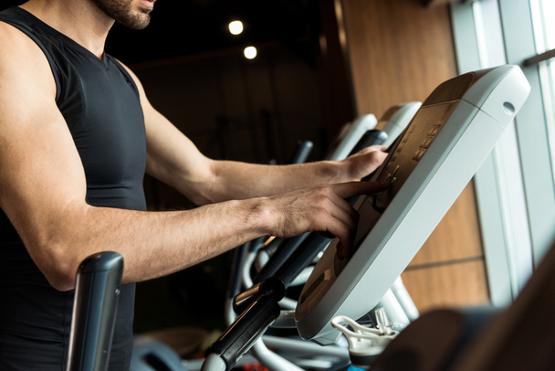 cropped view of man in sportswear pointing with finger at exercise bike in gym  - 写真・画像