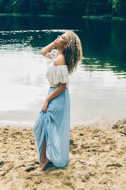 Curly woman in stylish dress posing on sandy lakeshore  - Valokuva, kuva