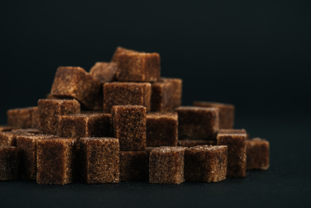 pila de dulces cubos de azúcar moreno sin refinar sobre fondo negro
  - Foto, Imagen