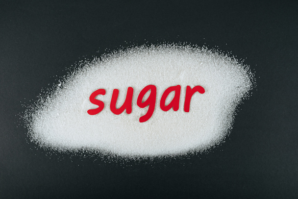 ylhäältä näkymä paperi leikattu sana sokeri valkoinen sokeri kiteet mustalla pohjalla
 - Valokuva, kuva