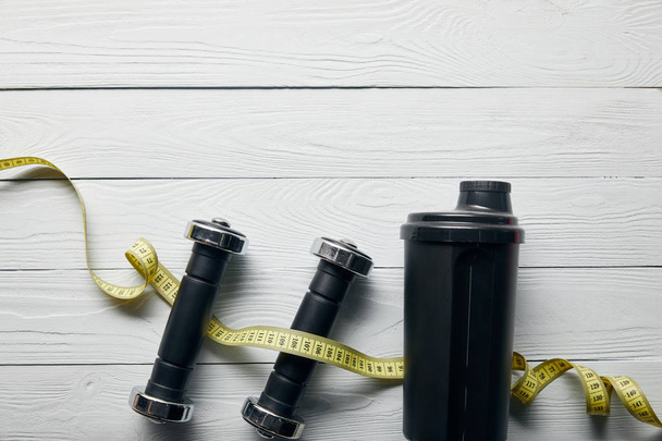 top view of black shaker cup, measuring tape and dumbbells on wooden white background with copy space - Foto, Imagem