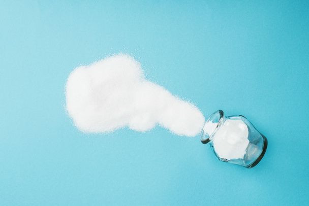 Κορυφαία όψη των κρυστάλλων λευκής ζάχαρης κοντά σε γυάλινο βάζο σε μπλε φόντο  - Φωτογραφία, εικόνα