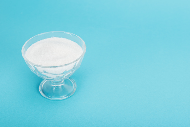 γυάλινο μπολ με λευκή κρυσταλλική ζάχαρη σε μπλε φόντο με χώρο αντιγραφής - Φωτογραφία, εικόνα