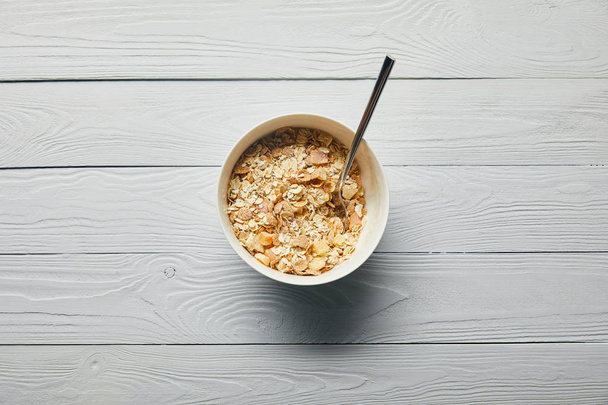 top view of breakfast cereal in bowl with spoon on wooden white background  - Zdjęcie, obraz