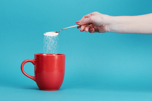 cropped view of woman adding sugar into red cup on blue background - Photo, Image