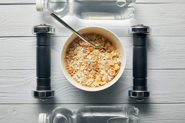 flache Liege mit Frühstückszerealien in Schüssel, Flaschen mit Wasser, Hanteln auf weißem Holzgrund - Foto, Bild
