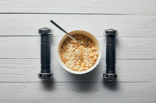 flat lay with breakfast cereal in bowl and dumbbells on wooden white background - Photo, image