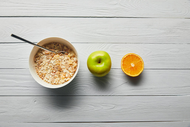 flache Lage mit Frühstückszerealien in Schüssel, Apfel, Orange auf weißem Holzgrund - Foto, Bild