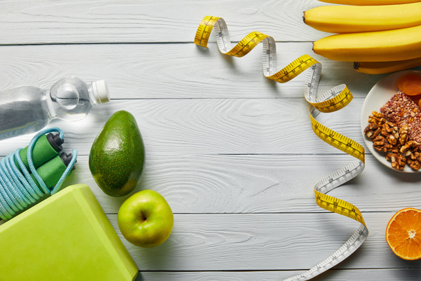 top view of diet food near measuring tape and sport equipment on wooden white table with copy space - Foto, Imagem