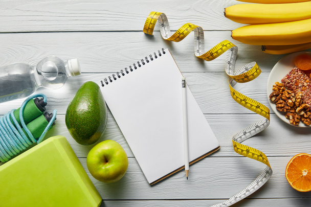 top view of diet food near measuring tape, notebook and sport equipment on wooden white background - Foto, imagen
