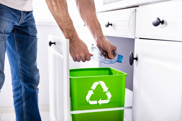 Alhainen osa mies heittää tyhjä muovipullo kierrätysastia keittiössä
 - Valokuva, kuva