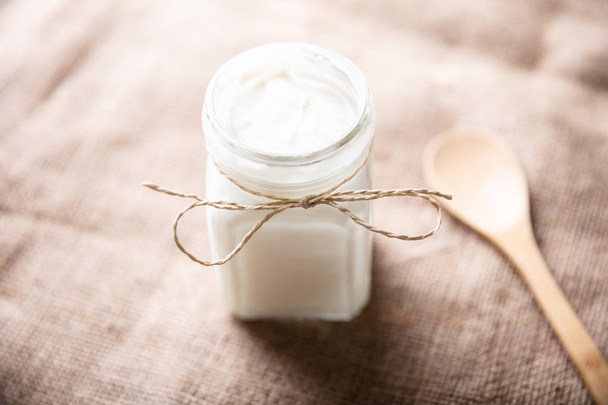 An Opened Jar With Yogurt Near Wooden Spoon Over Sack Cloth - Foto, Imagen