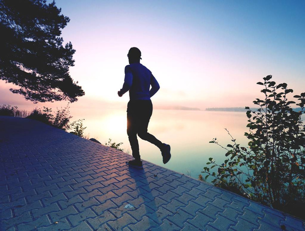 Ο άνθρωπος που τρέχει στο πεζοδρόμιο shore λίμνη κατά την Ανατολή ή το ηλιοβασίλεμα  - Φωτογραφία, εικόνα
