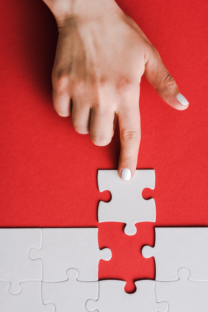 Draufsicht der Frau, die mit dem Finger auf Puzzleteile in der Nähe von miteinander verbundenen weißen Puzzleteilen auf Rot zeigt - Foto, Bild