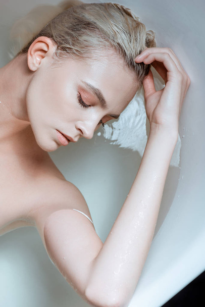 top view of nude woman with closed eyes in clear water in bathtub - Foto, afbeelding