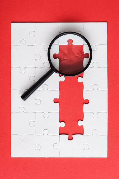 top view of magnifying glass near white puzzle pieces on red  - Photo, Image