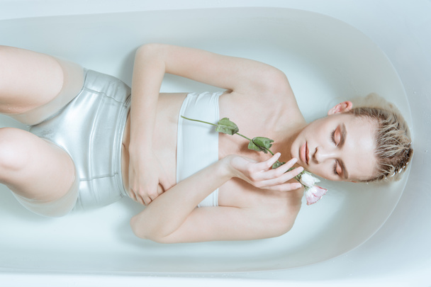 vista dall'alto della tenera donna con gli occhi chiusi che tiene delicatamente il fiore in acqua trasparente nella vasca da bagno
 - Foto, immagini