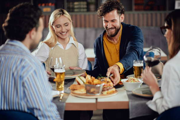Multiethnic przyjaciół siedzi w restauracji, picie alkoholu, rozmowy i po hamburgery na obiad. - Zdjęcie, obraz