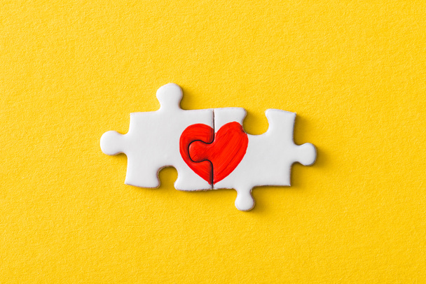 top view of connected jigsaw puzzle pieces with drawn red heart isolated on yellow  - Photo, Image