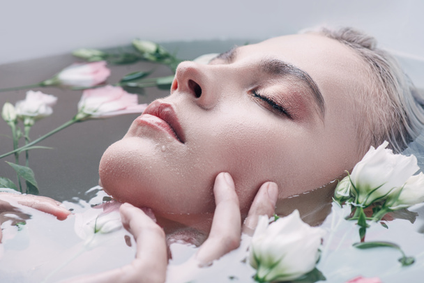 piękna kobieta z zamkniętymi oczami leżącą w jasnej wodzie z kwiatami  - Zdjęcie, obraz