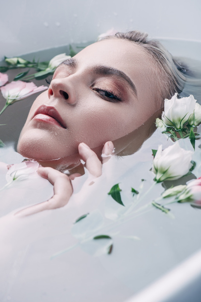 beautiful woman lying in clear water with flowers and looking at camera - Photo, Image