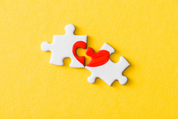 Draufsicht auf Puzzleteile mit gezeichnetem roten Herz isoliert auf gelb  - Foto, Bild