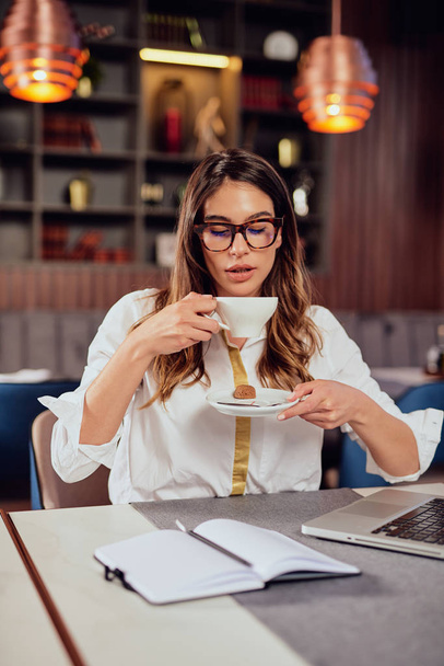 Jovem mulher de negócios caucasiana bebendo café enquanto sentada no café
. - Foto, Imagem