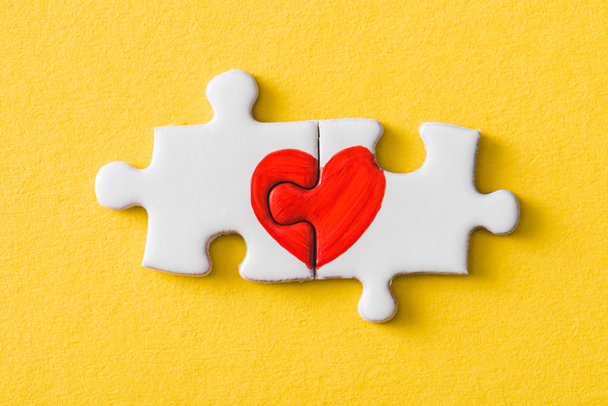 top view of connected puzzle pieces with drawn red heart isolated on yellow  - Photo, Image