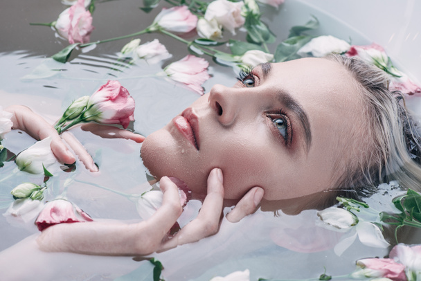 beautiful woman lying in clear water with flowers in white bathtub and looking away - Foto, Bild