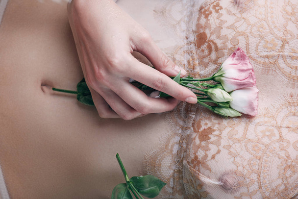 cropped view of wet woman in lace underwear holding flowers  - 写真・画像