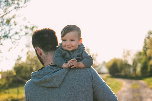 Cute baby boy on his dad's shoulders walking on the road outdoors, sensitivity to nature concept - Photo, image