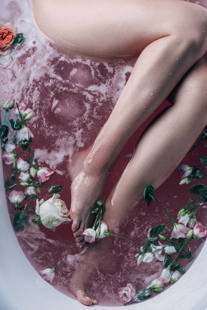 top view of barefoot female legs in pink water with flowers - Foto, immagini