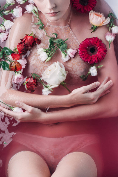 cropped view of sexy woman in beige lingerie in pink water among flowers - Fotografie, Obrázek