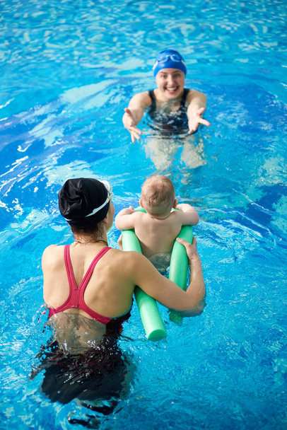 保護のためのプールヌードルで小さな子供の水泳を教えるインストラクター - 写真・画像