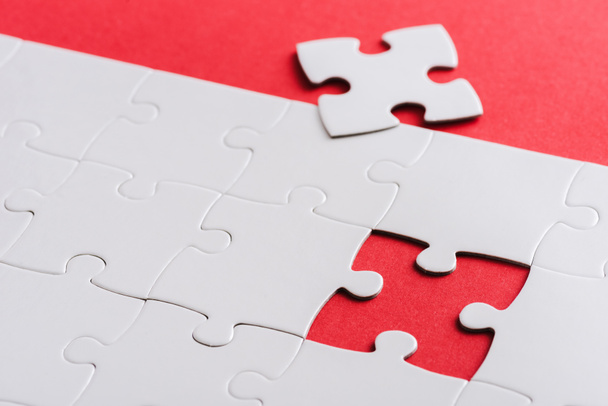 selective focus of unfinished white puzzles near separate piece isolated on red  - Fotografie, Obrázek
