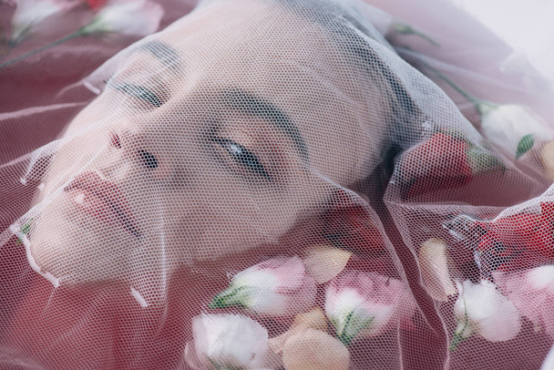 mooie vrouw bedekt met witte mesh doek in roze water met rozenblaadjes  - Foto, afbeelding