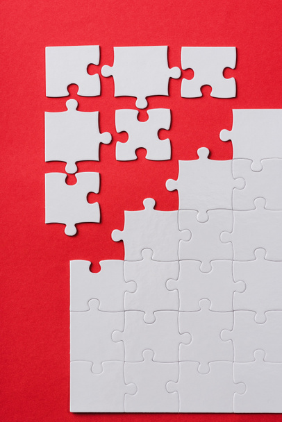 top view of white connected and separate jigsaw puzzle pieces isolated on red  - Fotó, kép