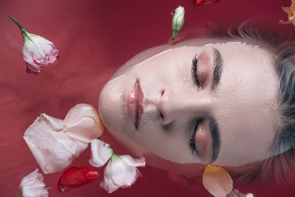 バラの花びらとピンクの水で目を閉じた美しい女性のトップビュー  - 写真・画像