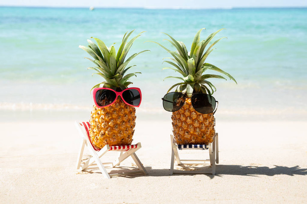 Two Whole Pineapple With Red And Black Sunglasses On Deck Chair At Beach - Фото, изображение