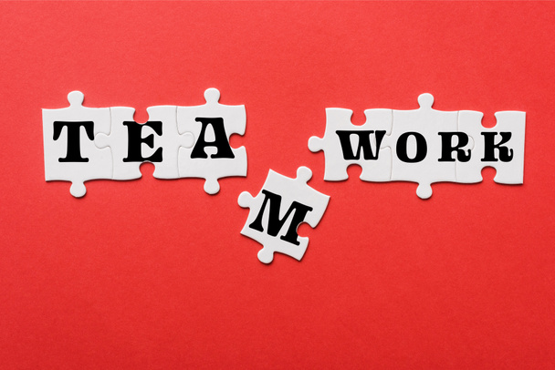 top view of white connected jigsaw near puzzle piece with teamwork lettering isolated on red  - Photo, Image
