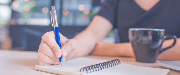 Mujer mano está escribiendo en un bloc de notas con un bolígrafo en la oficina
. - Foto, imagen