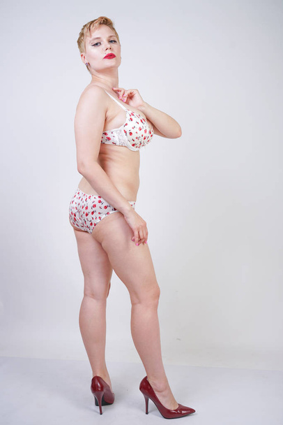 curvy caucasian short hair woman posing in cute white lingerie with red flowers print in the studio alone - Photo, Image