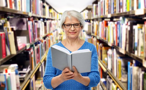 senior woman in glasses reading book at library - Zdjęcie, obraz