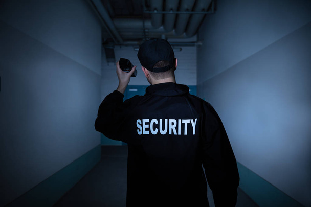 Πίσω όψη ενός αρσενικού φύλακα ασφαλείας με φακό που στέκεται στο διάδρομο - Φωτογραφία, εικόνα