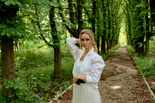 Blonde woman walks alone along the chestnut alley in the city park. Young woman modern portrait. - Photo, Image