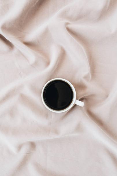 Coffee mug on silk pink blanket. Minimal flat lay, top view background. - Foto, afbeelding