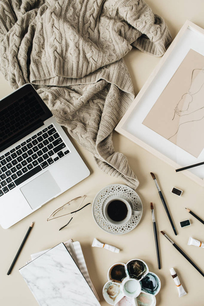 Watercolor painter home office desk workspace on beige background. Coffee cup, laptop, plaid, paint brushes, painting, watercolor. Flat lay, top view art blog, social media, website concept composition. - 写真・画像