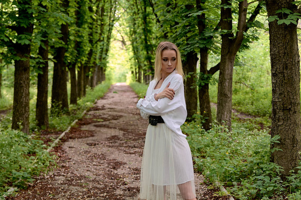 Blonde woman walks alone along the chestnut alley in the city park. Young woman modern portrait. - Photo, Image