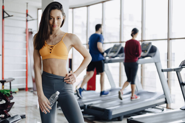 young attractive girl in the gym drinking water on the background of treadmills - Photo, Image